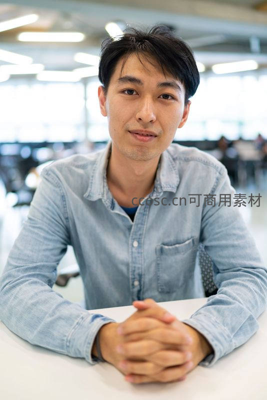 青年男子双手交叠坐于桌前微笑直视镜头
