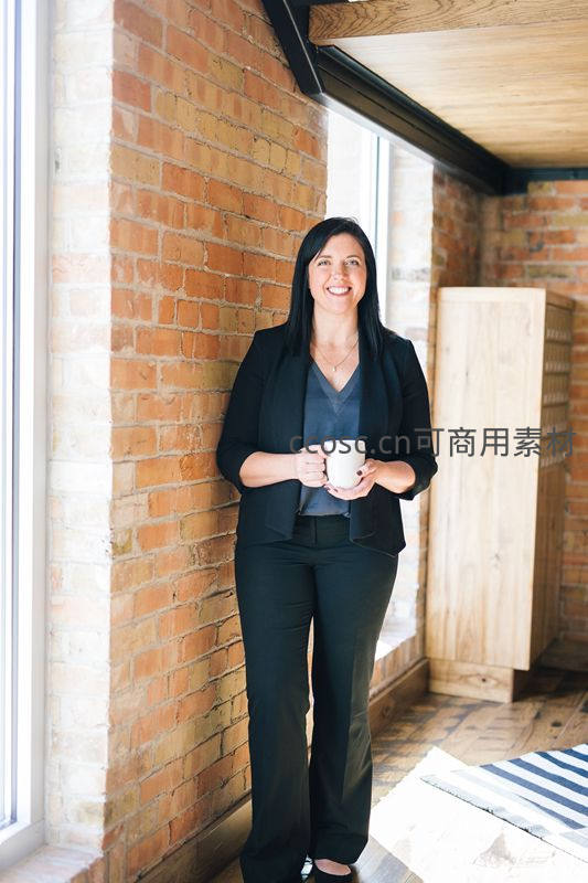 职业女性窗边持杯微笑，砖墙背景