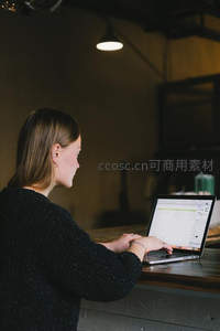 女性侧身专注电脑屏幕，昏黄灯光下