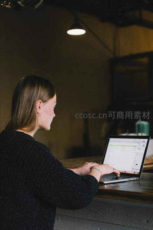 女性侧身专注电脑屏幕，昏黄灯光下
