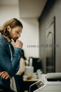 长发男士沉思站在打印机旁