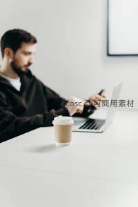 咖啡杯前景中男子使用手机电脑