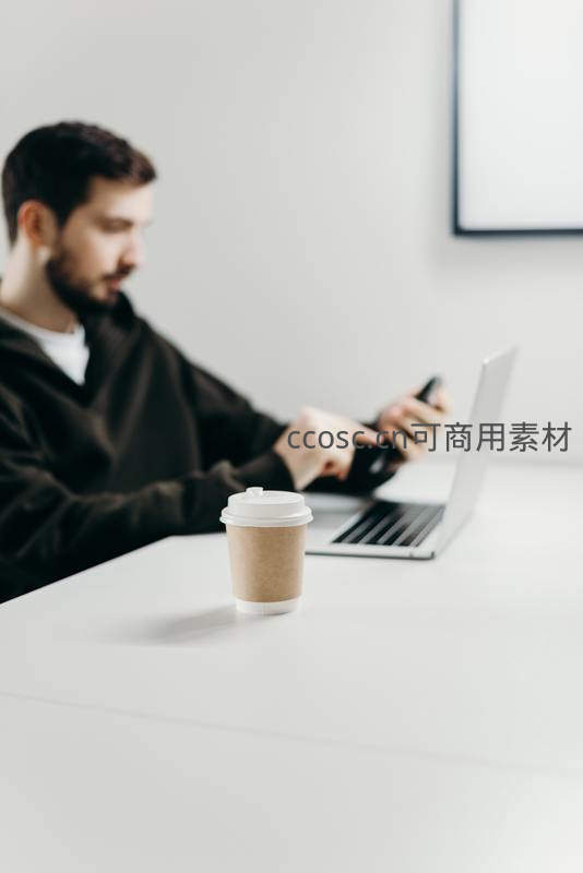 咖啡杯前景中男子使用手机电脑