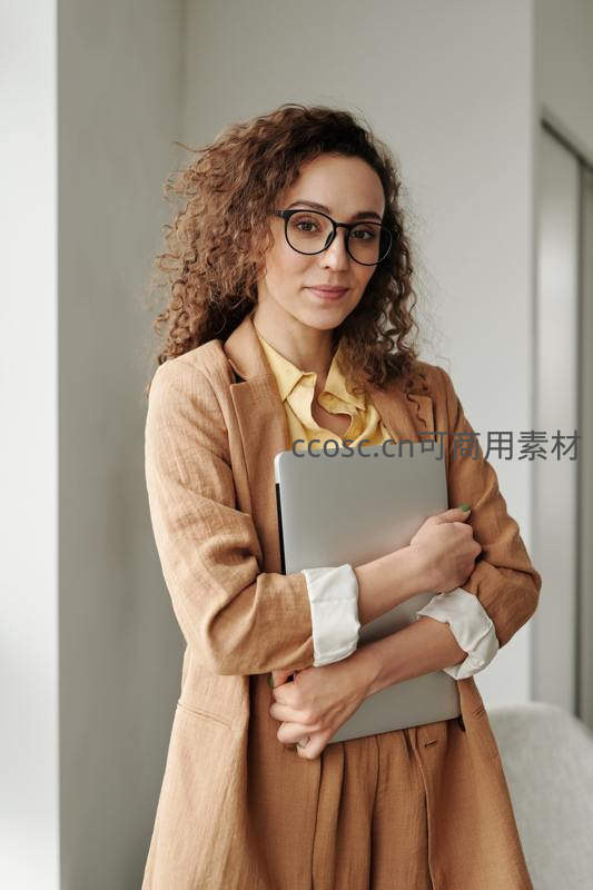 戴眼镜的卷发女性抱着笔记本电脑微笑