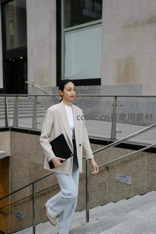 职业女性手拿文件夹走在现代办公楼台阶