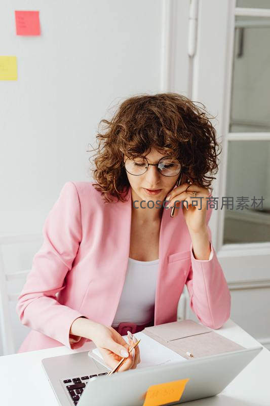 粉色西装女白领边打电话边做笔记