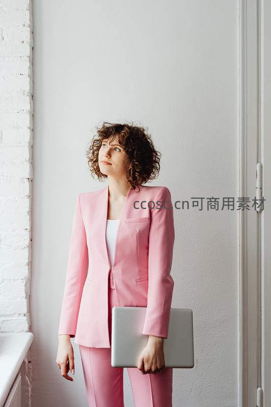 穿粉色西装的女白领手持笔记本电脑