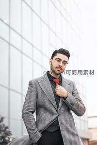 时尚男士调整领带站在现代建筑前