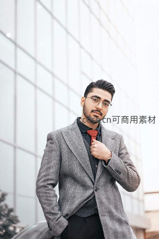 时尚男士调整领带站在现代建筑前
