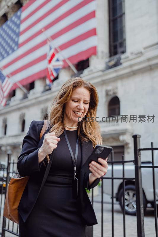 女性在华尔街前兴奋查看手机消息