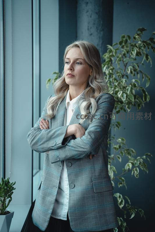 女经理双臂交叉望窗外沉思
