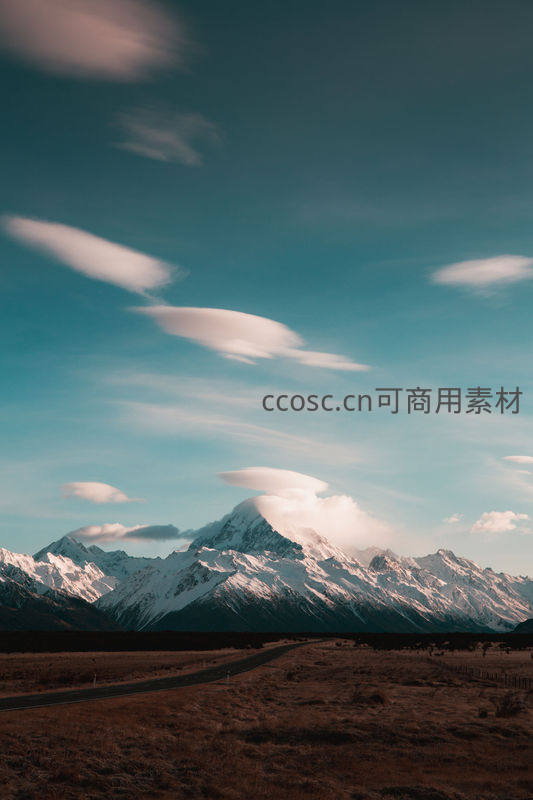 公路延伸向雪峰，帽状云朵舞天际
