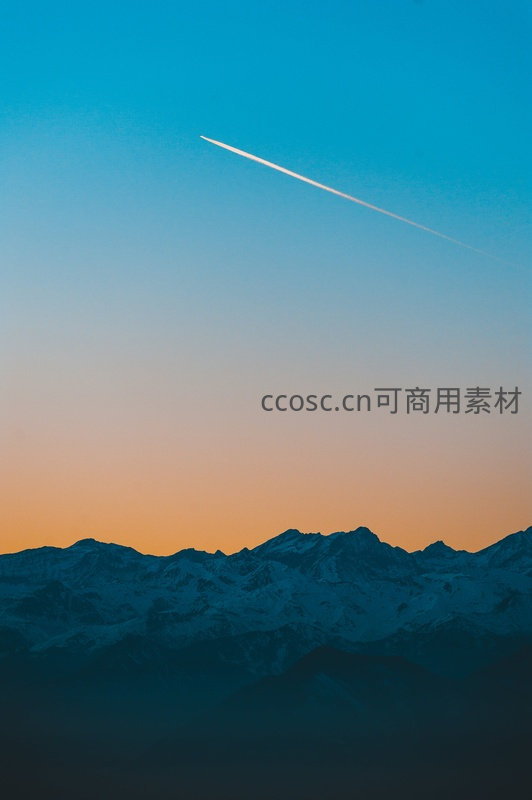 雪山剪影映衬日落彩霞与飞机航迹