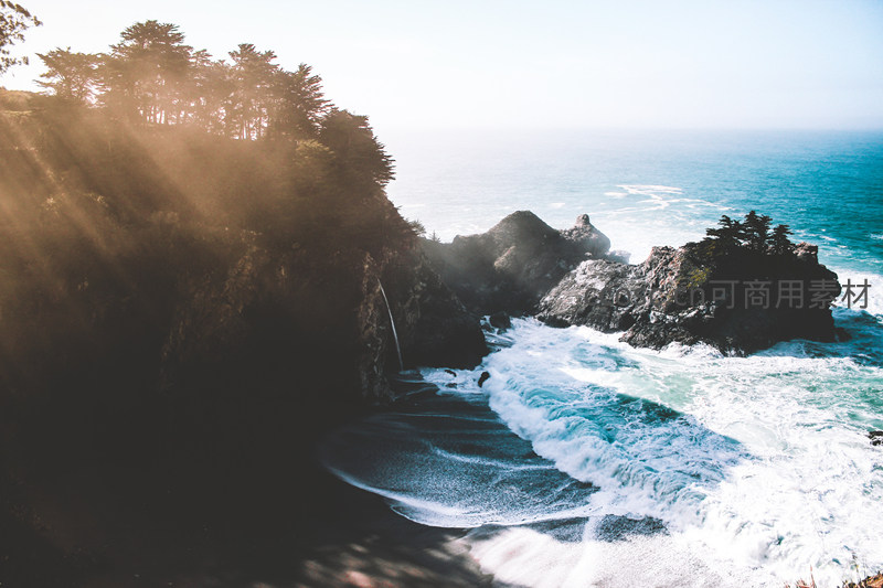 阳光穿透海岸悬崖，海浪拍打岩石