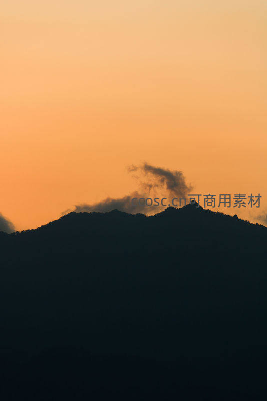 橙黄霞光中云雾缭绕的山峰剪影