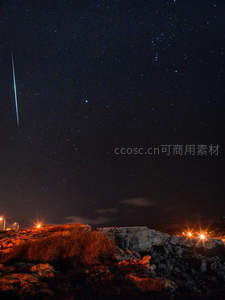 陨石划破夜空，岩岸灯火映衬星轨