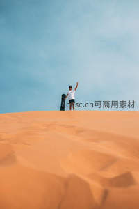 沙丘之巅，少年手举滑板迎蓝天