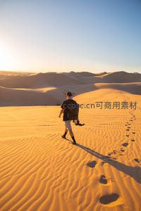 夕阳下的旅人，背包行走在金色沙海
