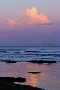 海岸夕照映云影，浪花轻吻礁石滩