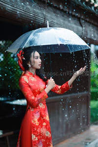 红裙女子雨中撑伞，轻触飘落水珠