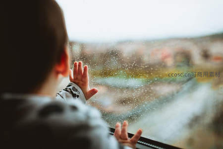 孩童望窗外雨，手触玻璃留印
