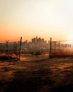 铁丝网围栏后夕阳映照的城市剪影