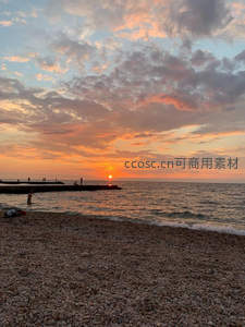 晚霞满天石滩边，游人驻足赏落日