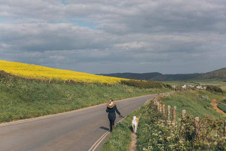 女子牵狗漫步乡间公路旁金黄油菜花田