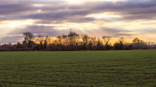 夕阳穿透云层洒在田野与树梢之上