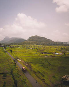 航拍视角下的绿色田野与山路巴士