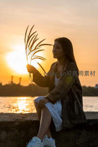 夕阳下女子手持芦苇微笑