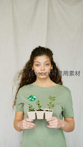 女子身着环保T恤，手捧三盆绿植直视镜头
