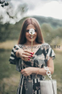 女子手持蒲公英遮面微笑