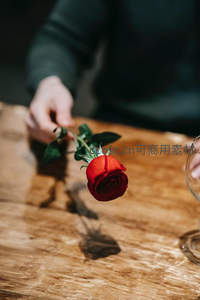 手中轻握一支红玫瑰置于木桌