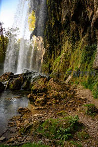 飞瀑垂崖溅水花，岩壁青苔映碧潭
