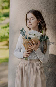 少女怀抱纸包白花倚柱而立，清新自然