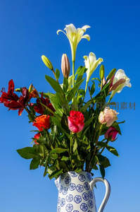蓝天映衬下花瓶中的百合与玫瑰