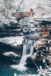雪中古桥观瀑，红衣人影添暖意
