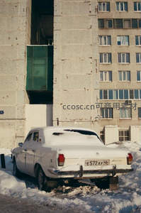 老式轿车覆雪停靠苏联风格公寓楼前