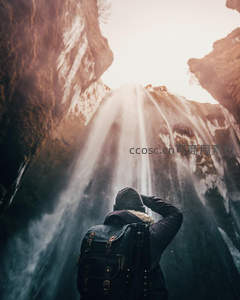 旅者仰望水帘洞，背包行囊追光影