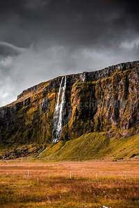 阴云密布下，山崖瀑布倾泻于草原之上