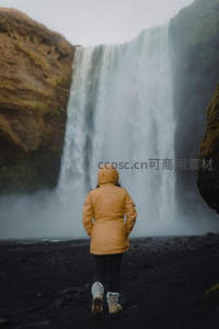 黄衣旅人踏黑沙走向冰岛壮丽瀑布