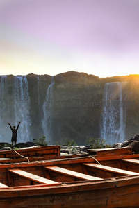 夕阳下瀑布前张开双臂的旅人