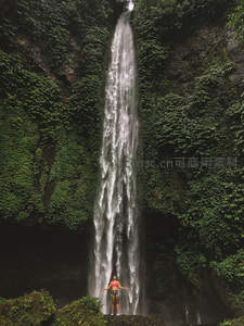 绿意瀑布前张开双臂的游客