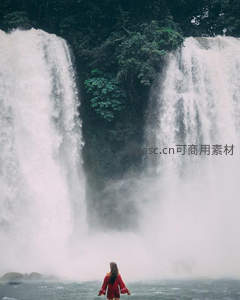 红衣女子背对镜头，置身水雾弥漫的巨瀑前