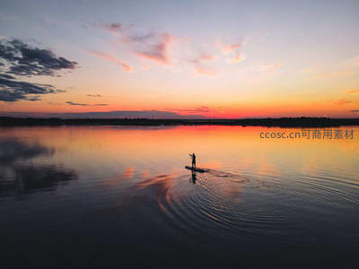 夕阳桨板剪影，水面涟漪染霞光