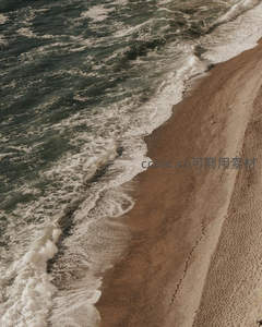 鸟瞰沙滩与海浪交界处，足迹蜿蜒如诗