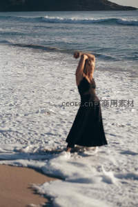 黑裙女子海边漫步，浪花轻抚脚踝