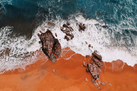航拍视角下海浪拍打红沙滩与礁石的壮丽景象