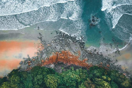 绿林、红滩与碧海交汇的海岸全景航拍图